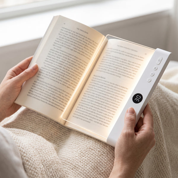 The reading light lying on a paperback page, held in two hands, to show its size